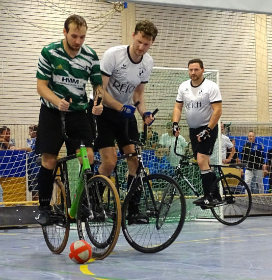 Martin Egarter und Thomas Kieferle während eines Radballspiels,
                          wobei Thomas Kieferele den Gegenspieler, welcher den Ball besitzt, vom Tor abschirmt.