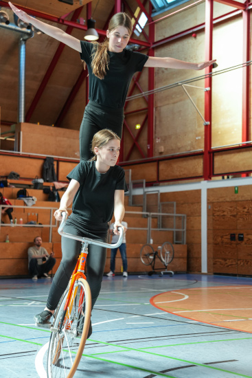 Foto einer Figur im Kunstrad, bei der zwei Personen gleichzeitig auf einem Fahrrad fahren, wobei eine davon aufrecht auf dem Sattel steht.